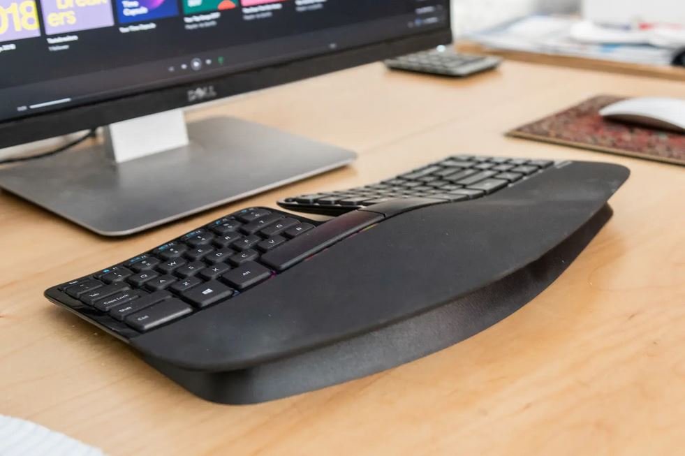 Un gros plan sur le clavier ergonomique Microsoft Sculpt posé devant un écran d'ordinateur, sur un bureau.
